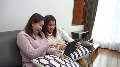Friends Laughing at Tablet on Couch Indoors