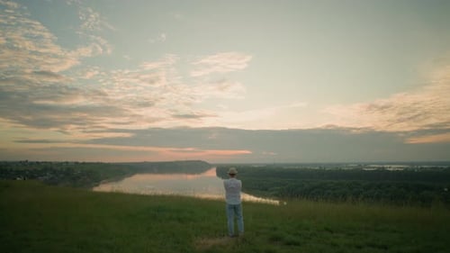 Man Standing By Lake in Grassland at Sunset Reflecting on Tranquil Scene
