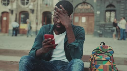 Urban Scene Captures Man Showing Distress While Engaging with Mobile Device Amid Worn Steps and