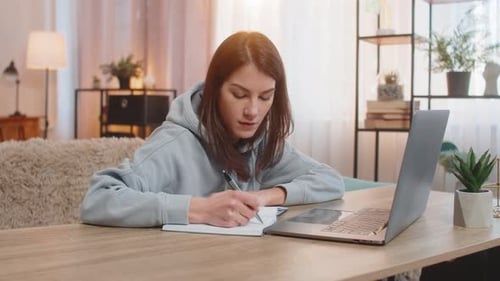 Woman Writing in Notebook Next to Laptop