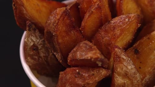 Deep fried potato wedges or french fries rotate in paper cup. Footage can be used to advertise