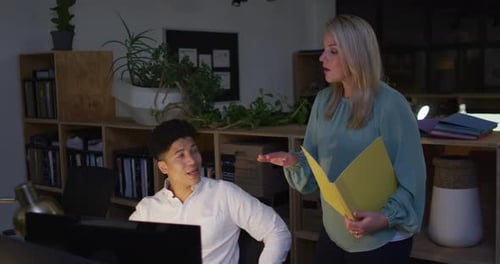 Une femme caucasienne et un homme biracial collaborent sur un projet d'entreprise dans un bureau, travaillant tard