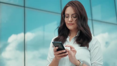 Young Business Woman Texting on a Mobile Phone While Standing on the Street Next to a Modern