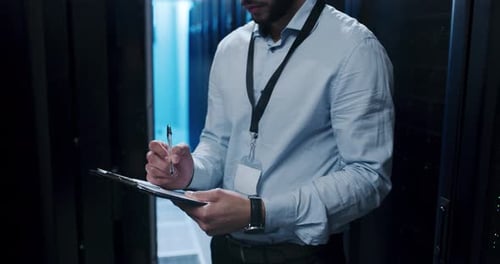 4K-Videomaterial eines jungen Mannes, der Notizen macht, während er in einem Serverraum arbeitet