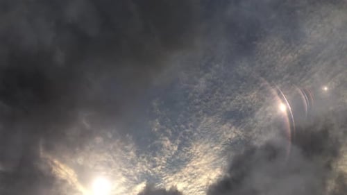atmosphere, the sun with rays flares among the dark clouds in the blue sky.
