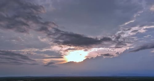 Dramatic Sunset Illuminates Cloudy Sky Over Tranquil Landscape at Dusk