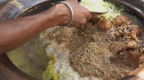 Unrecognized hand of person serving Traditional Indian Chicken Biryani from Large Pot or handi