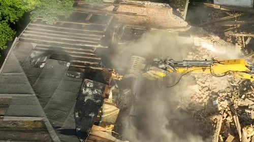 Aerial shot capturing the moment of building demolition as heavy tears down structures, producing la