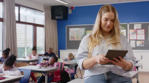 In school, female teacher smiling while students writing at their desks in classroom