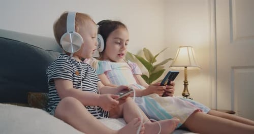 Children with Headphones Using Mobile Phones on Bed