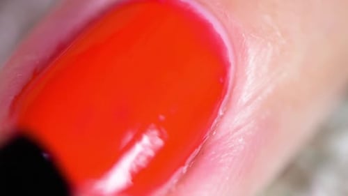 Amateur applying protective layer of lacquer on the red nail polish. Macro close-up