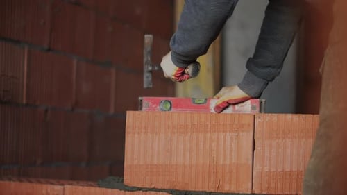 Bricklayer Adjusting Brick Position with Hammer and Spirit Level