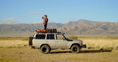 Woman Stands Atop Car in Rural Mountain Landscape