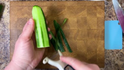 Peeling a fresh cucumber against the background of a wooden cutting board. Top view.