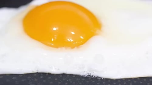 Zeitlupen-Nahaufnahmevideo eines Eies, das auf einer heißen Pfanne gebraten wird, Vertikales Video