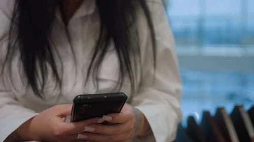 Close Up of Woman Using Smartphone with Polished Nails and Tattoo in Indoor Setting