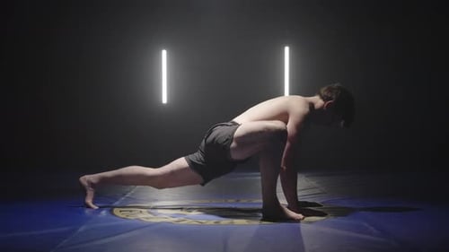 young athletic man doing stretches yoga position, side view in dark studio setting
