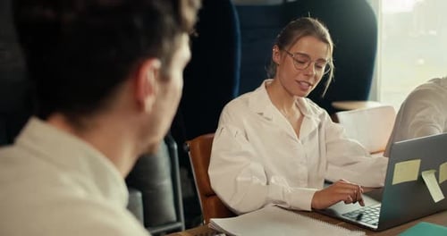 Une fille blonde avec des lunettes dans une chemise blanche communique avec un employé en chemise blanche assis