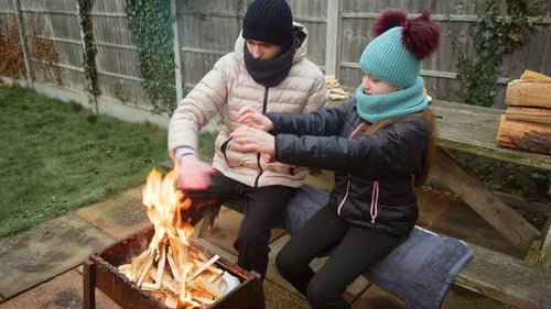 Brother and Sister Warming Hands By Fire Enjoying Heat From Burning Wood Uplifting Family Moments