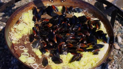 Les moules sont versées dans une grande casserole et cuites sur un feu ouvert à l'extérieur, avec de la vapeur montante et une cuisson rustique