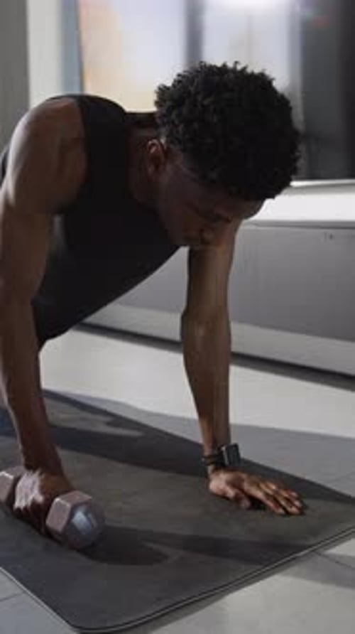 Man Doing Dumbbell Rows on Yoga Mat Indoors