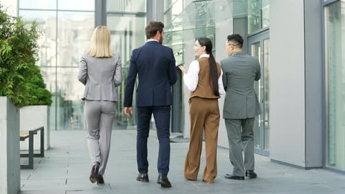Rear back view of a business team people walking near office center chatting. Diverse Group