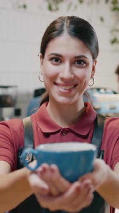 A Cheerful Barista Holds a Vibrant Blue Cup Joyfully in a Cozy Warm Coffee Shop