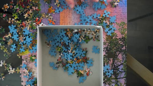 Scooping up puzzle pieces and placing them back in the storage box. Overhead view