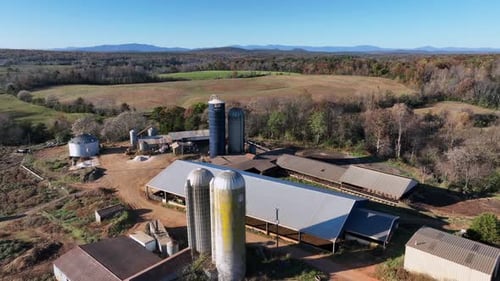 Aerial descend shot of silo storage on farm surrounded by agricultural fields and colored trees in A