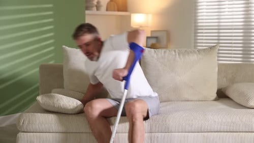 Injured Man with Crutch Sitting on Couch Indoors