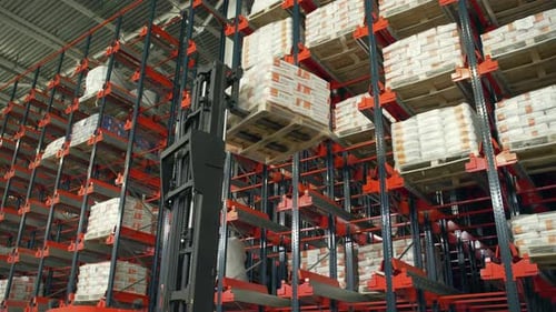Warehouse Worker Lifting Goods with Forklift in Large Distribution Center