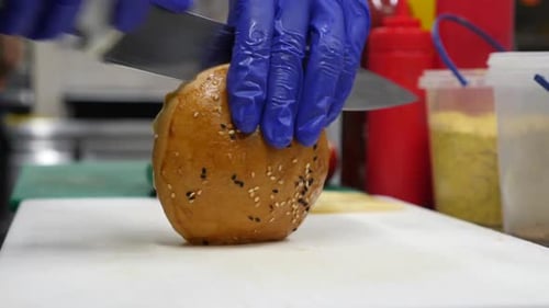 Gloved Hands Cutting Burger Bun in Kitchen