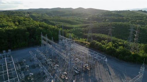 Aerial drone view of large electrical substation surrounded by forested hills and high voltage