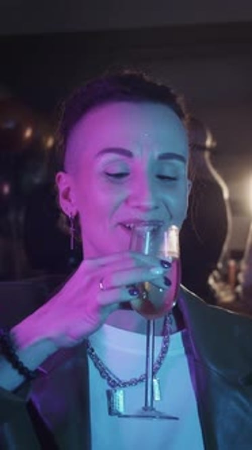 Woman Drinks Champagne at Party Under Neon Lights