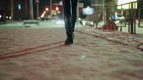 Woman in Black Leather Trousers and Boots Walking at Night on Snowy Street