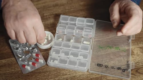 Man Organizes Pills into Pill Organizer on Table