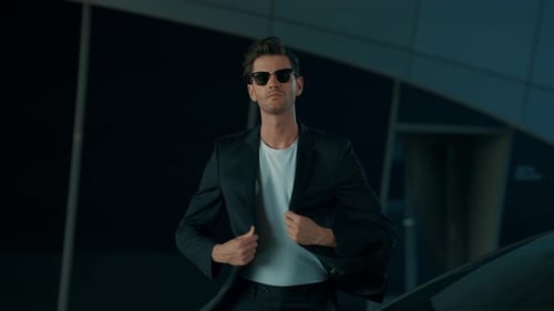 Homem com óculos de sol parado perto de um carro em um local moderno