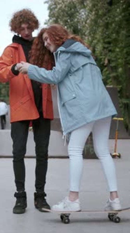 A Couple is Happily Enjoying Their Time Skateboarding Together in a Vibrant Urban Park Setting