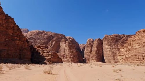 White sand below river valley of Wadi Rum, epic cliffs rise against blue sky