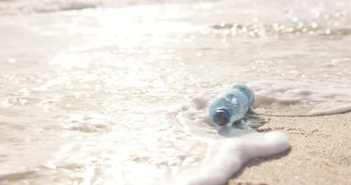 Beach, ocean and plastic bottle in sand for pollution, litter and trash in sea for global warming