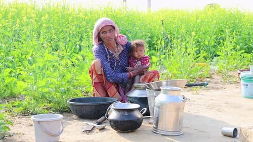 poor malnutrition village women living below poverty line holding baby with mustard fields behind
