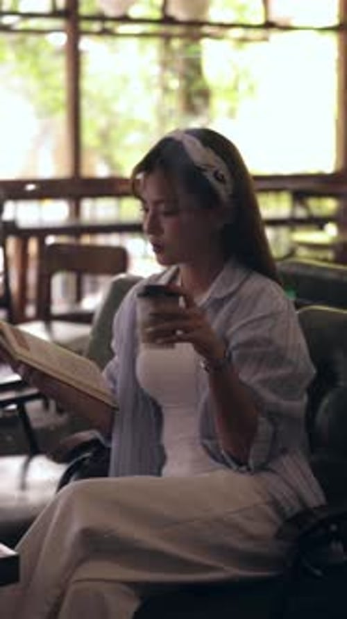 Young Asian Woman Reading and Sipping Coffee in a Cozy Cafe