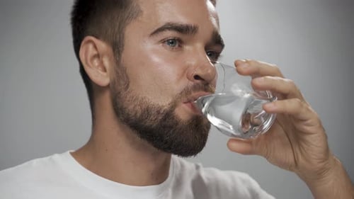 Schöner Mann trinkt Süßwasser vor grauem Hintergrund