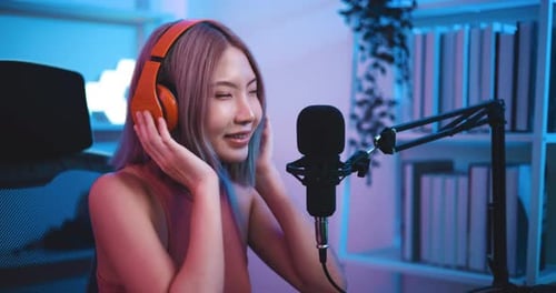 Young Asian woman influencer wearing headphones talking into a microphone while recording a radio