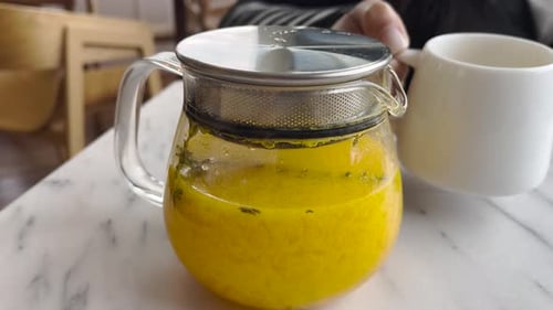 Clear Teapot Filled with Bright Yellow Herbal Drink
