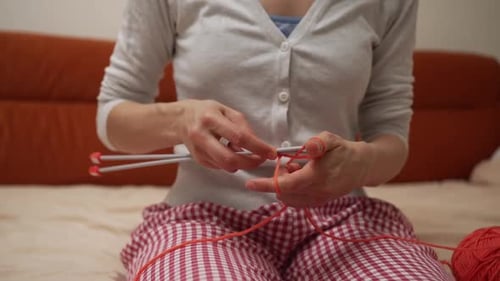 Woman Knitting with Orange Yarn on Bed at Home