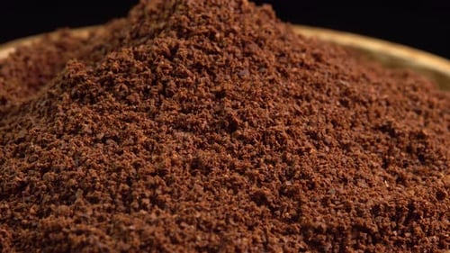 Café molido natural que gira en cuenco de madera sobre fondo negro. Montón de café molido fino