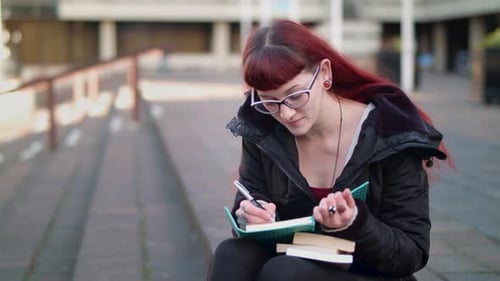 Woman Writing in Notebook Outdoors on College Campus