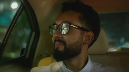 Businessman Riding in Taxi at Night and Smiling