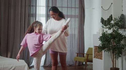 Woman Helping Girl Stretch Leg in Bright Room